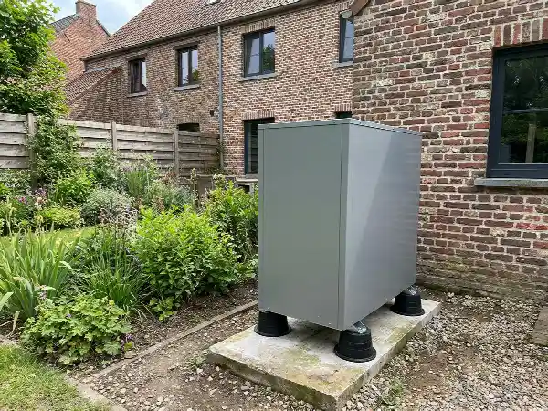 Buitenunit van een lucht-waterwarmtepomp op trillingsdempers achter een bakstenen woning